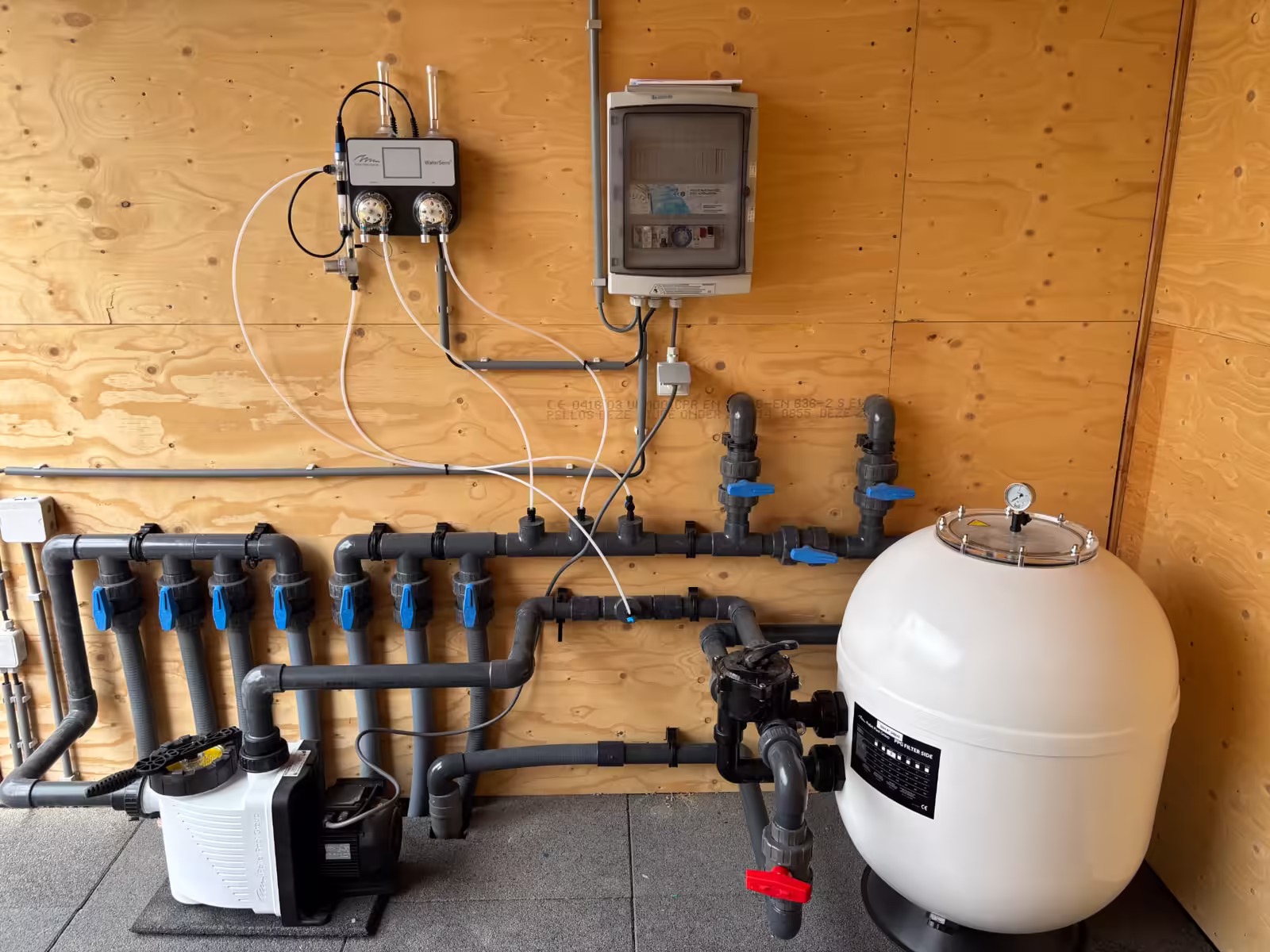 Vers geplaatste zwembadinstallatie met doseersysteem, PVC-verdeling en zandfilter tegen een houten wand