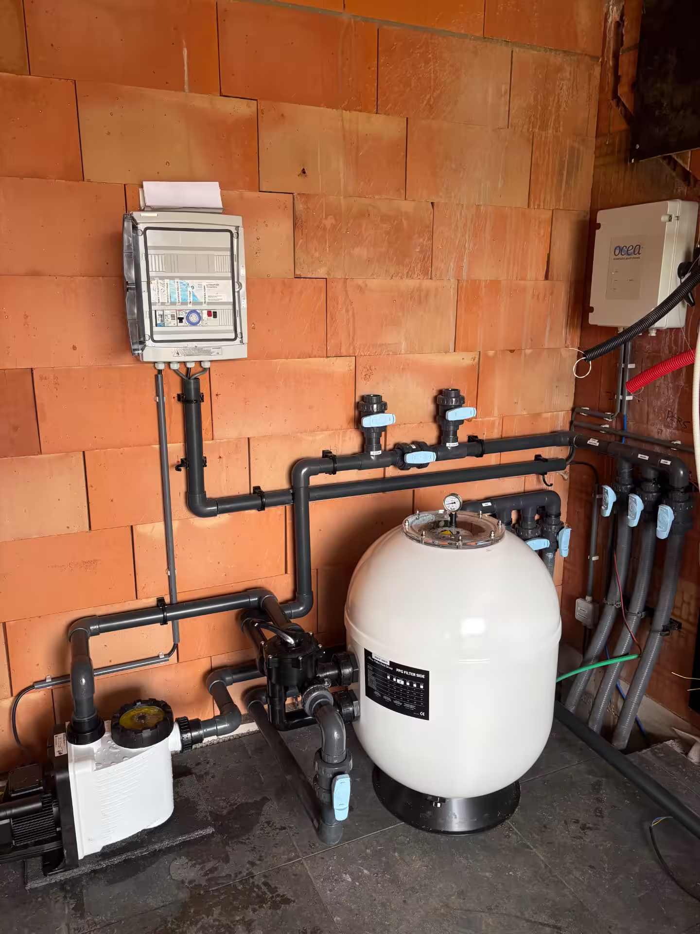 Zwembadtechniek in ruwbouw met leidingwerk, zandfilter en OCEA-besturing tegen oranje metselwerk