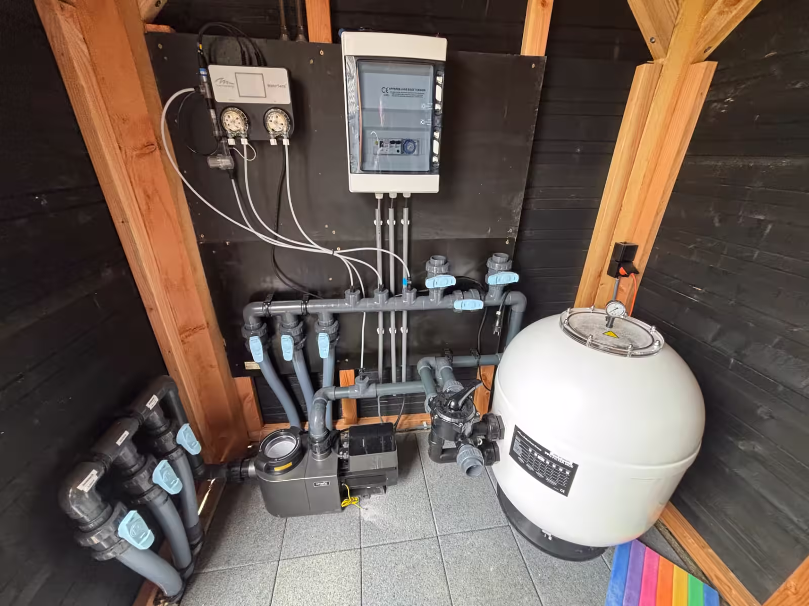 Compacte technische ruimte in een houten berging met doseersysteem, PVC-leidingwerk en zandfilter