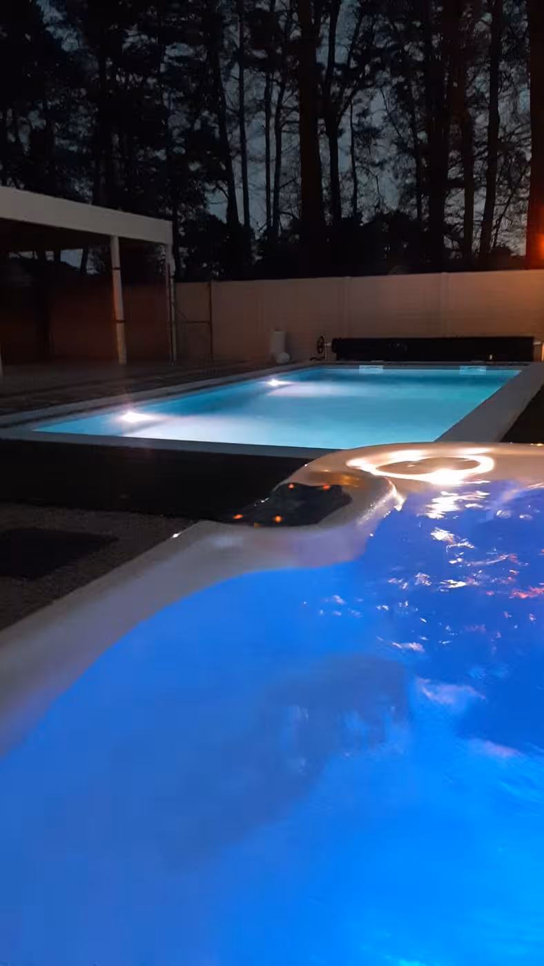 Sfeerbeeld bij avond: het verlichte bad met aangrenzende spa
